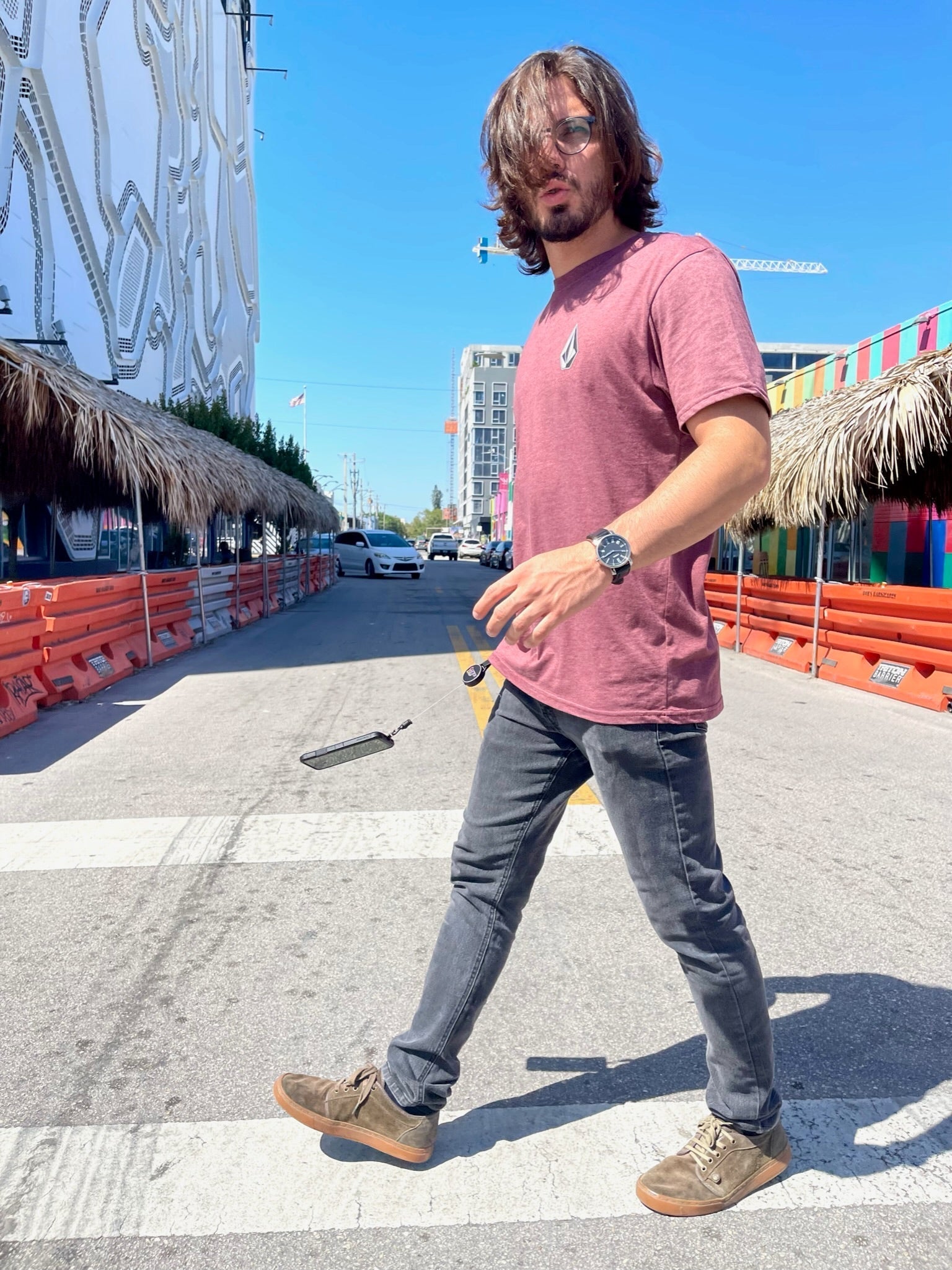 Jose walking in a city crosswalk as phone falls, saved by ClutchLoop anti-theft phone tether