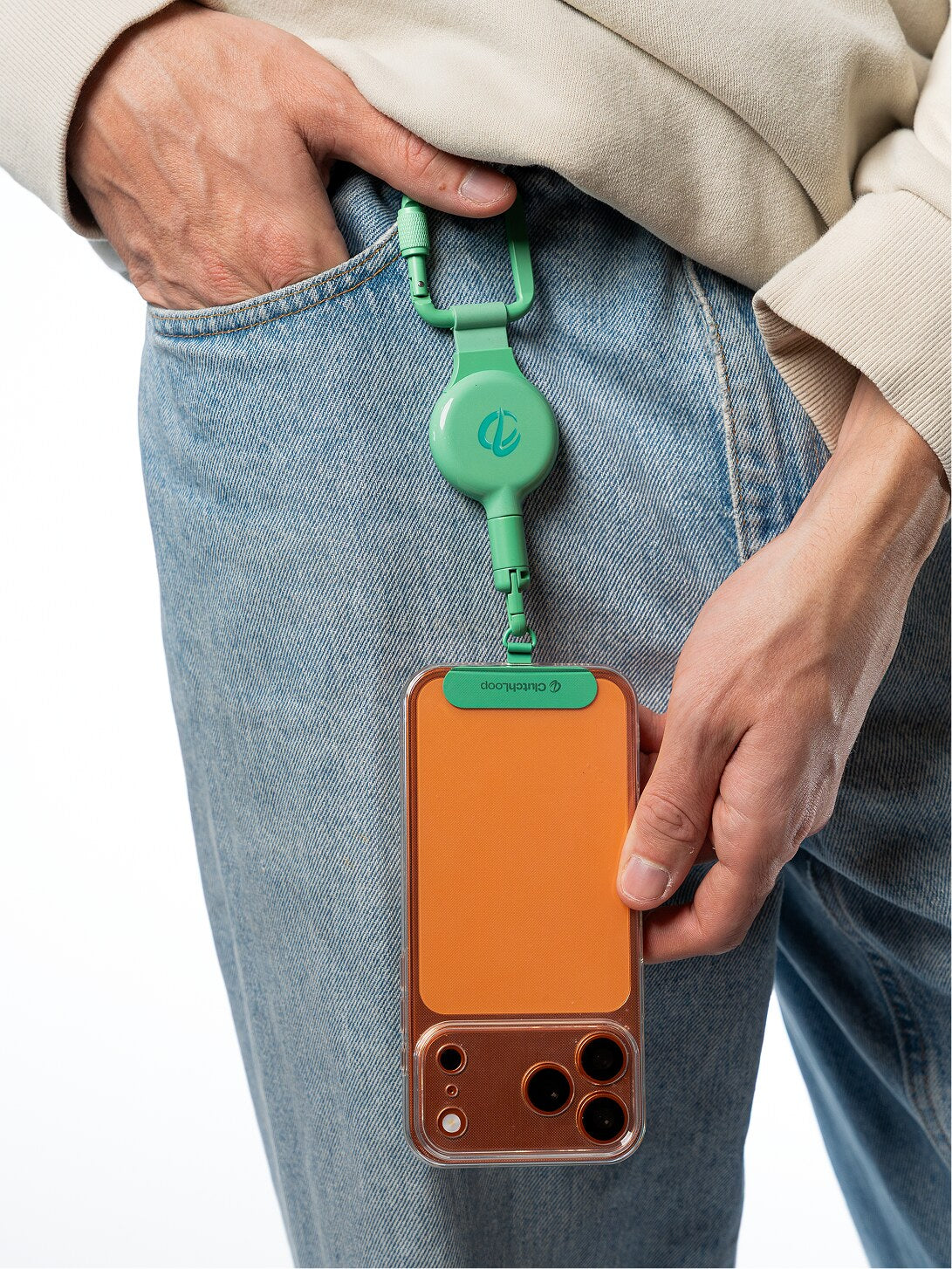 Matcha ClutchLoop clipped to light blue jeans holding an orange phone
